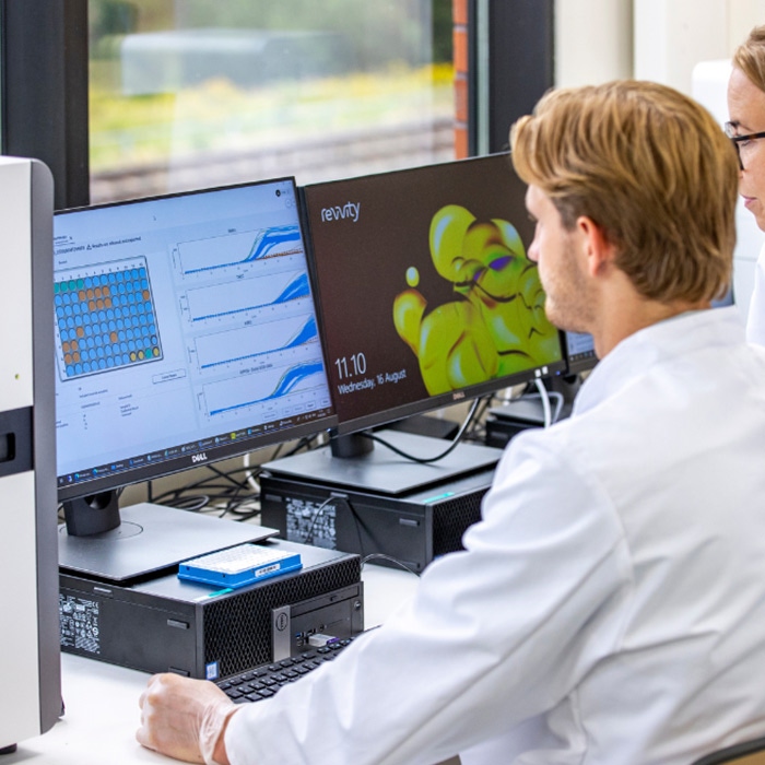 Lab scientist seated at a workstation next to an Eonis Q instrument while working on a computer.
